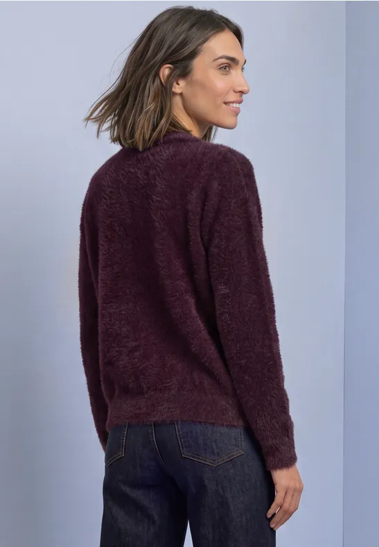 Frau in flauschigem lila Pullover und Jeans, von hinten seitlich fotografiert.