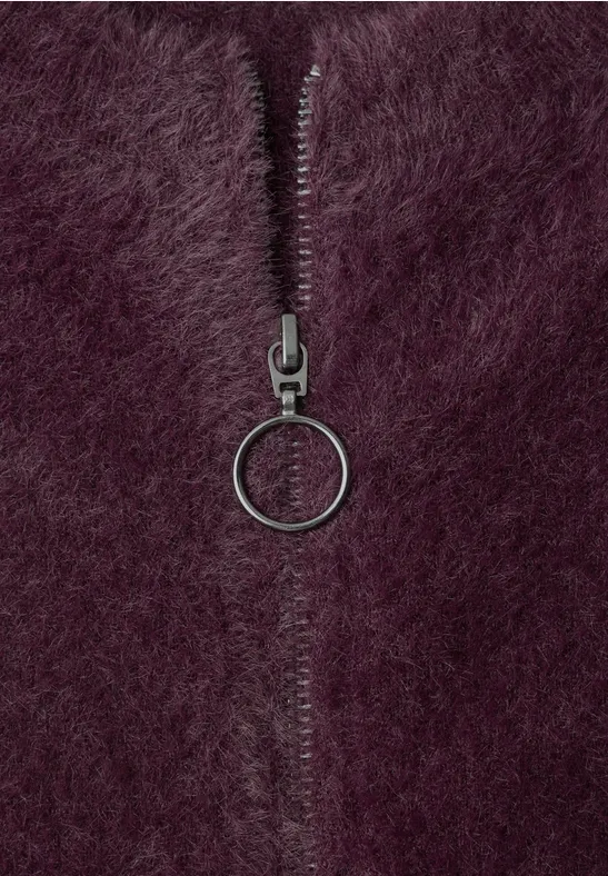 Nahaufnahme eines lila/plumfarbenen Pelzstoffs mit einem Reißverschluss und rundem Ring als Zipper.