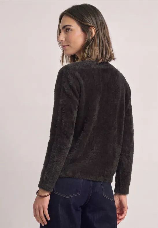 Frau in flauschigem, dunkelgrauem Pullover und dunkler Jeans, halb von hinten zu sehen