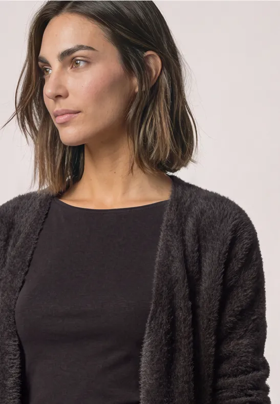 Eine Frau mit dunklem, flauschigem Cardigan und schwarzem Oberteil schaut zur Seite.