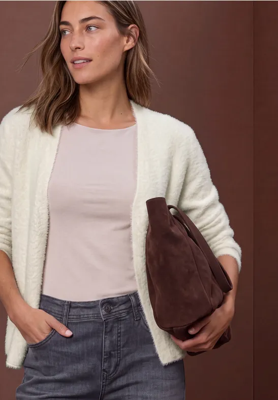 Frau in heller Strickjacke, rosa Shirt und Jeans hält eine braune Tasche unter dem Arm.