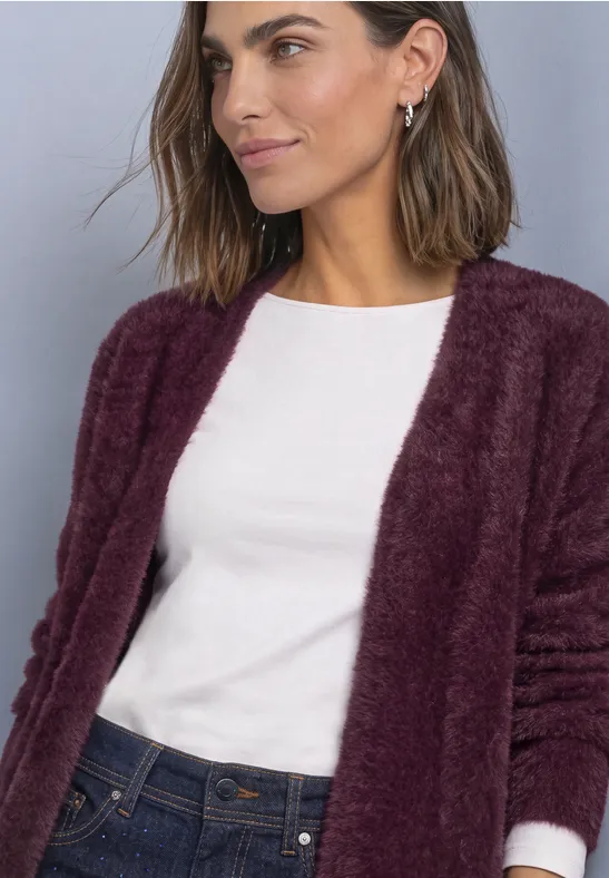 Eine Frau trägt eine flauschige, burgunderfarbene Strickjacke über einem weißen Shirt.