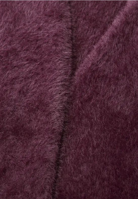 Nahaufnahme eines flauschigen, burgunderfarbenen Stoffes mit weicher, pelziger Oberfläche.