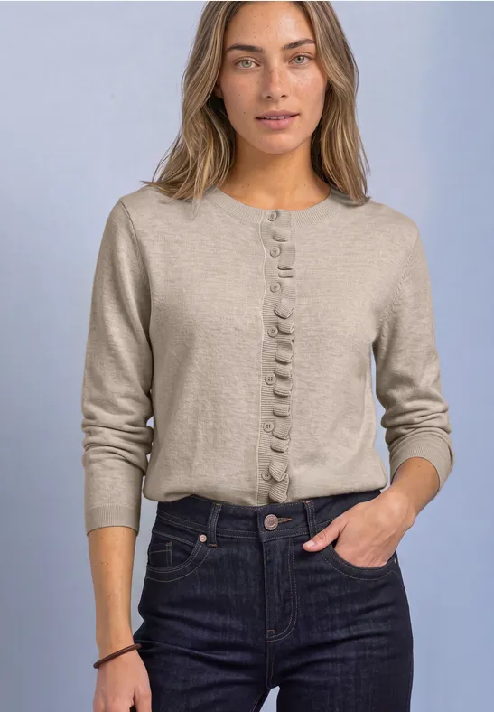 Eine Frau trägt eine beige Strickjacke mit Zierknöpfen und dunkle Jeans.