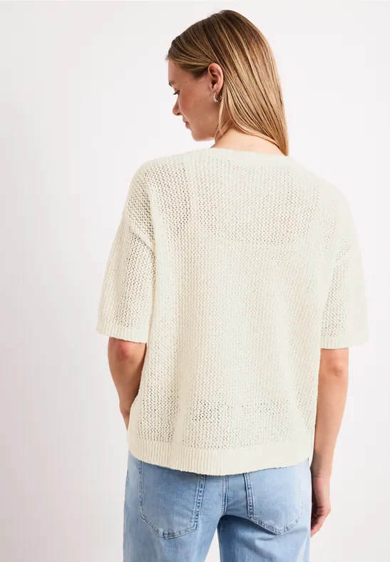 Vrouw van achteren in lichtgebreide top met korte mouwen en een spijkerbroek voor een witte achtergrond.