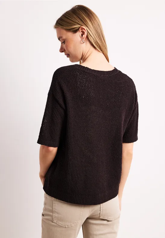 Femme aux cheveux blonds vue de dos, pull noir ample et pantalon clair.