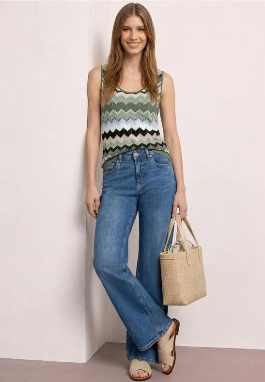 Frau im bunten Zickzack-Top, weitem Jeans, Sandalen und Beuteltasche.