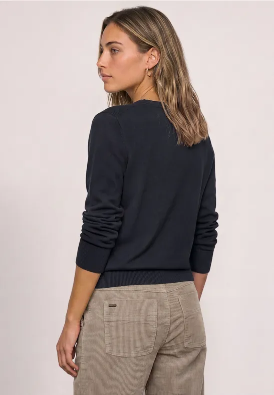 Achteraanzicht van een vrouw in een donkerblauwe trui en beige broek.