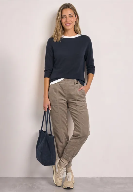 Vrouw in donkerblauwe trui, wit shirt, beige cargobroek, sneakers en bijpassende tas