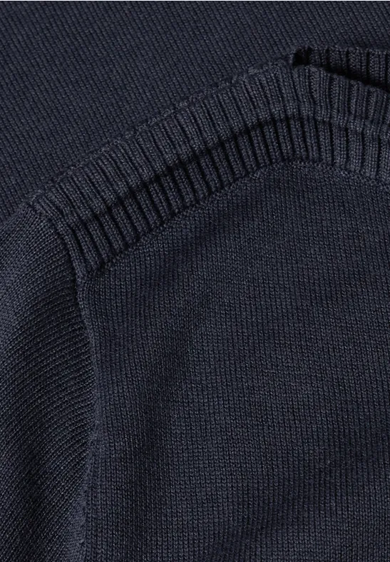 Close-up van een donkerblauwe gebreide trui met opgestikte zak en geribbelde boorden.