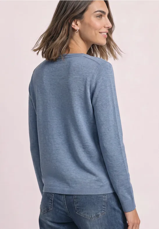 Frau von der Seite in lockerem hellblauen Pullover und Jeans.