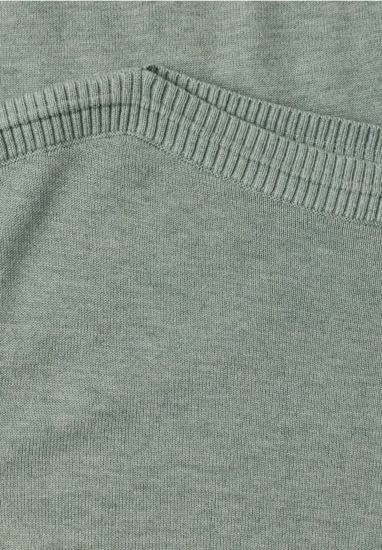 Nahaufnahme eines grünen Strickpullovers mit sichtbarer Naht und weichem Stoff.