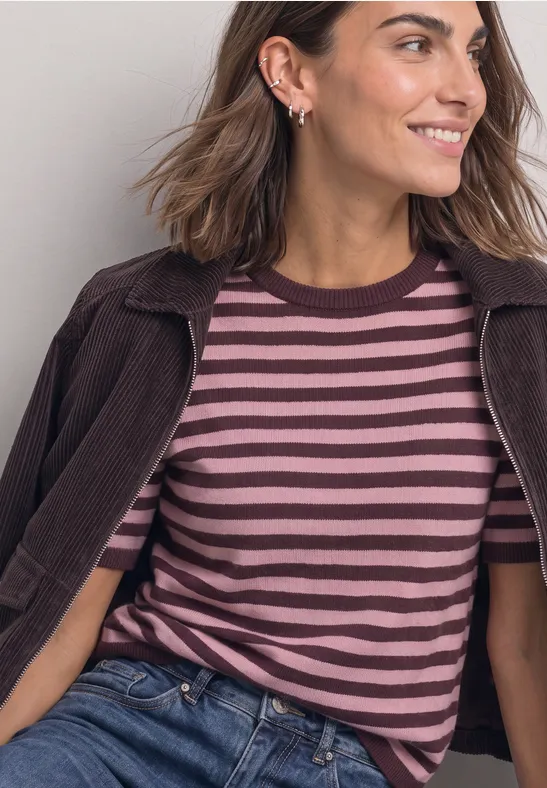 Frau in braun-rosa gestreiftem Shirt und Jacke lächelt seitlich.