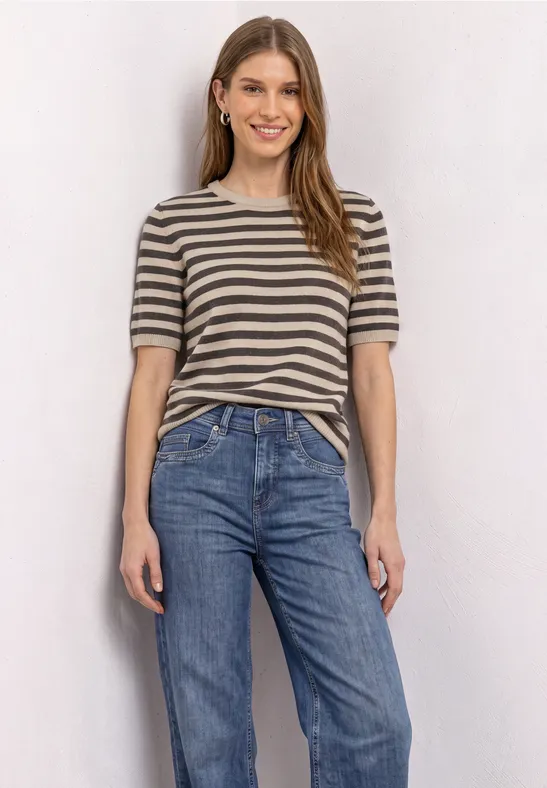 Eine junge Frau trägt ein gestreiftes T-Shirt und Jeans, sie lächelt entspannt.