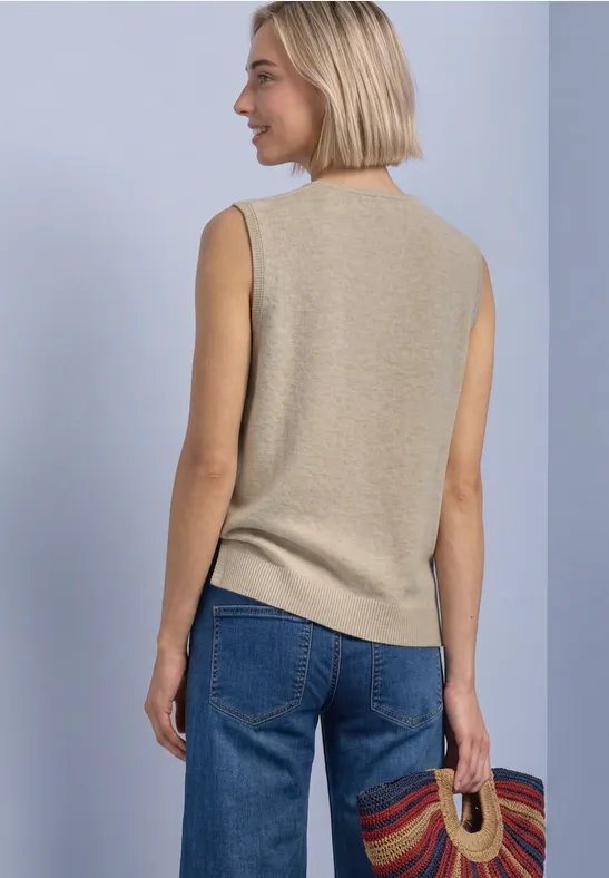 Frau von hinten trägt ein beiges ärmelloses Top, blaue Jeans und hält einen bunten Korb.