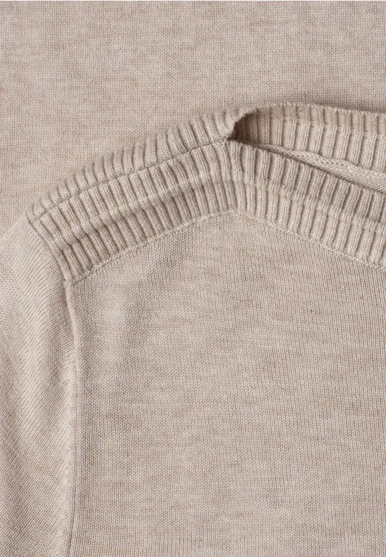 Nahaufnahme eines beigen Strickpullovers mit geripptem Halsausschnitt und Schulternaht.