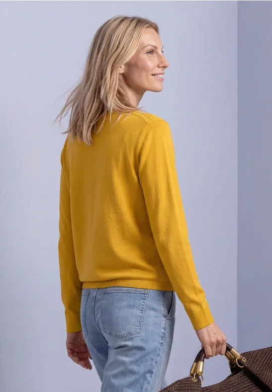 Frau in gelbem Pullover und Jeans hält lächelnd einen braunen Korb in der Hand.
