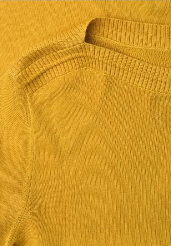Nahaufnahme eines senfgelben Strickoberteils mit Rundhalsausschnitt und feiner Struktur.