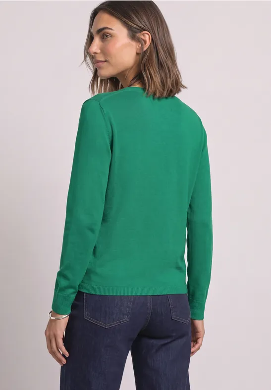 Frau von hinten in grünem Langarmshirt und Jeans, Kopf zur Seite gedreht.