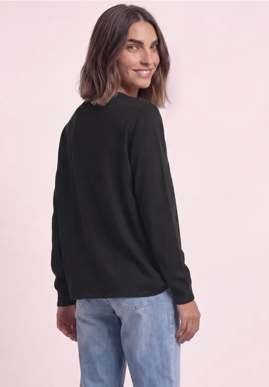 Eine Frau in schwarzem Pullover und blauer Jeans schaut über ihre Schulter.
