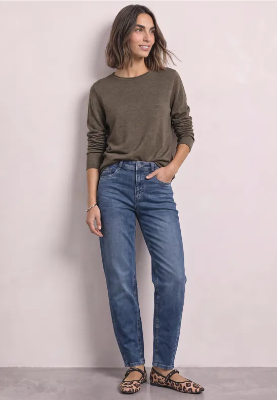 Vrouw in groene trui, blauwe jeans en luipaardprint ballerina's voor lichte achtergrond.