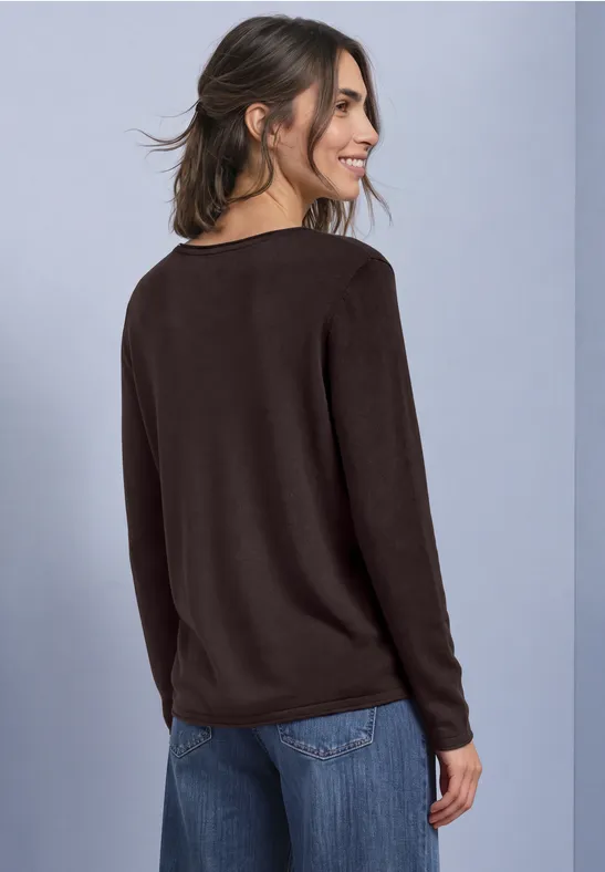 Frau in schwarzem Pullover und Jeans, die lächelnd über die Schulter blickt.