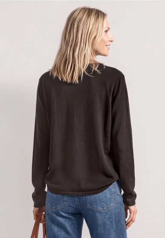 Eine Frau steht mit dem Rücken zur Kamera und trägt einen dunklen Pullover und Jeans.