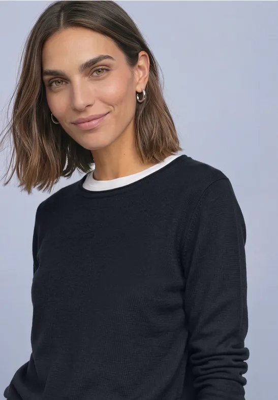 Eine lächelnde Frau mit braunen mittellangen Haaren, trägt schwarzen Pullover und weißen Kragen.