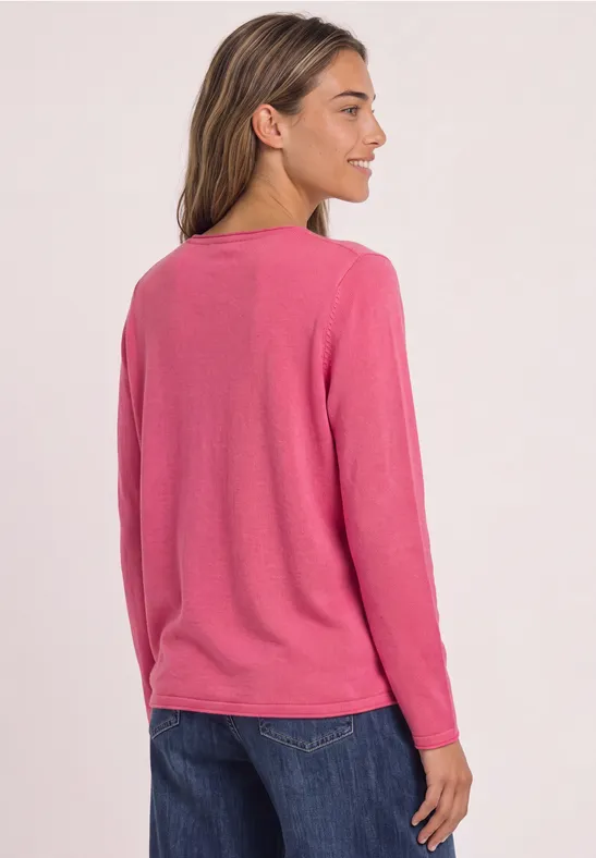 Frau von hinten mit rosa Langarmshirt und dunkler Jeans vor hellem Hintergrund.