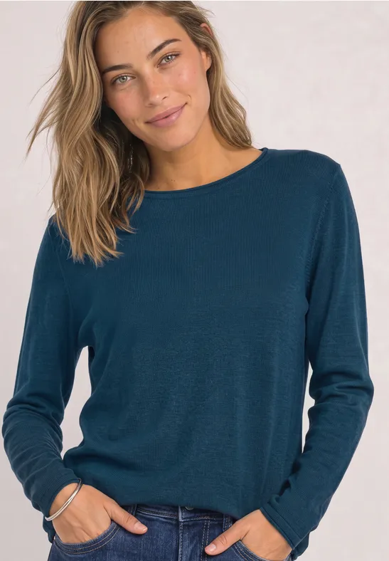 Junge Frau mit mittellangem hellbraunem Haar trägt einen blaugrünen Pullover und lächelt in die Kamera.
