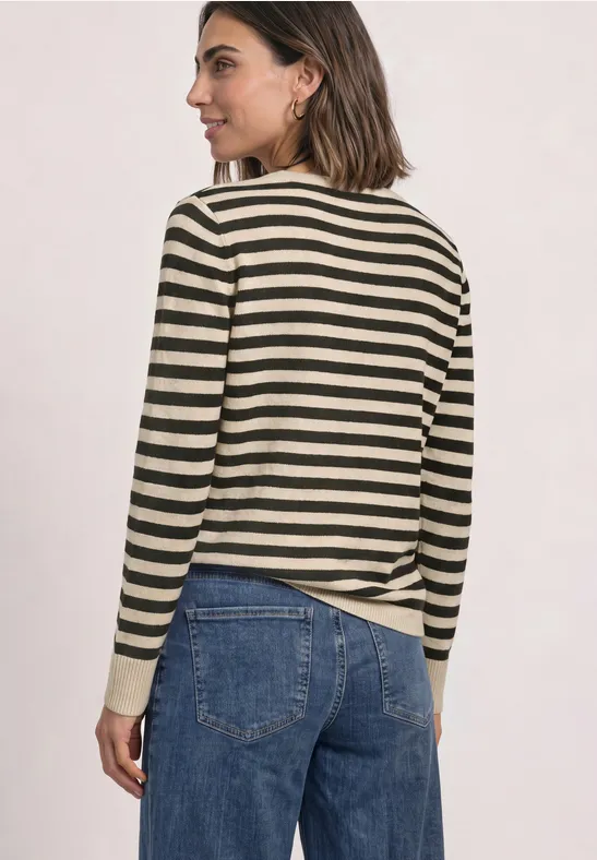Eine Frau von hinten trägt einen gestreiften Pullover in Schwarz-Beige und eine blaue Jeans vor hellem Hintergrund.