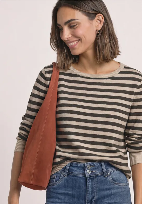 Eine lächelnde Frau mit kurzem Haar in gestreiftem Oberteil, Jeans und brauner Tasche.