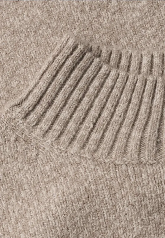 Gros plan sur un pull en maille beige avec col roulé côtelé.