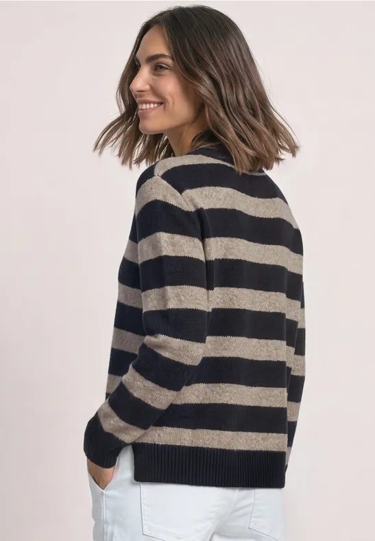 Frau mit schulterlangen Haaren und gestreiftem Pullover, seitlich stehend und lächelnd.