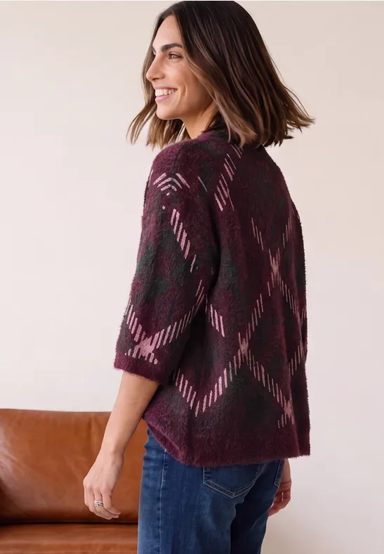 Frau im Profil mit bordeauxroter Strickjacke und dezentem geometrischem Muster, dazu Jeans.