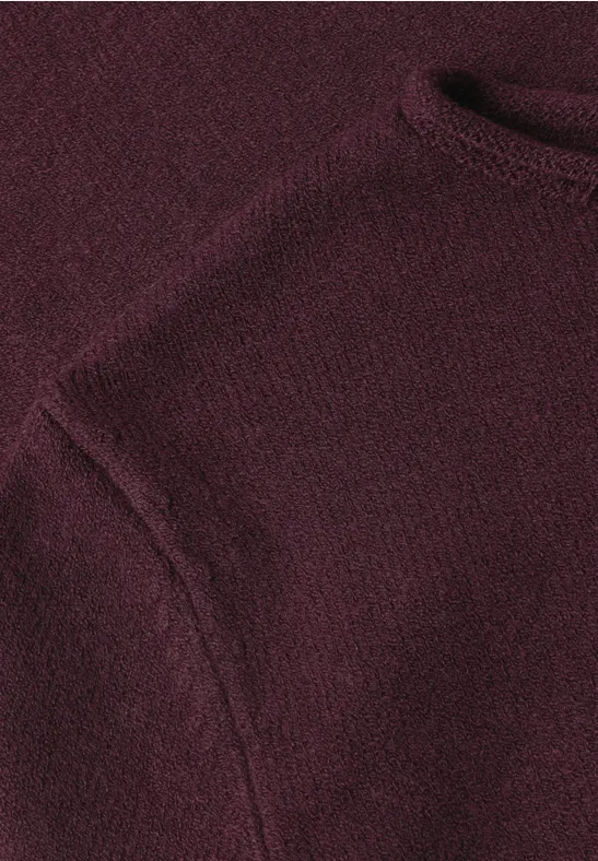 Nahaufnahme eines burgundroten Strickpullovers mit Schulterpartie und angerauter Textur.