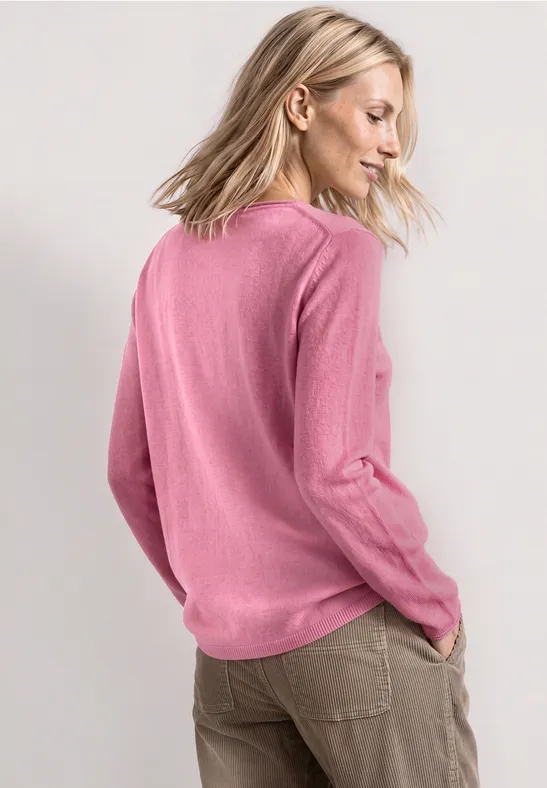 Blonde vrouw van achter gefotografeerd in een roze trui en kaki broek, hoofd zijwaarts gedraaid.