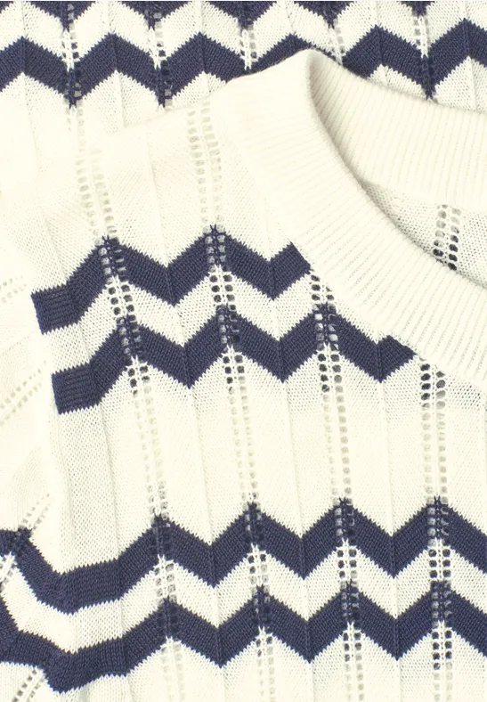 Nahaufnahme eines weißen Strickpullovers mit dunkelblauen Zickzack-Streifen.