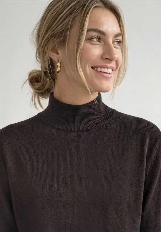 Femme souriante, chignon, pull à col roulé marron.