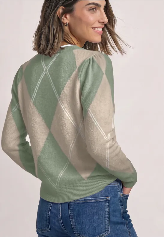 Vrouw in groen-beige argyle trui, glimlachend, kijkt over haar schouder.