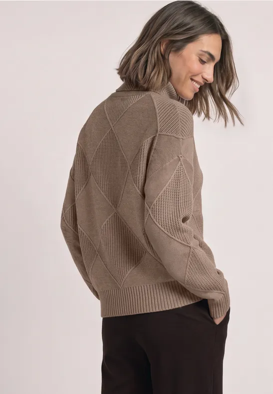 Frau in beigem Pullover mit Rautenmuster, Rückansicht, lächelnd.