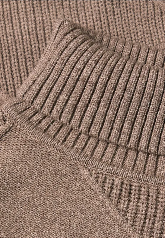 Nahaufnahme eines beigen, gerippten Rollkragen-Pullovers aus weichem Strick.