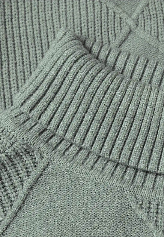 Nahaufnahme eines pastellgrünen Strickpullovers mit Rippenmuster und diagonaler Naht.