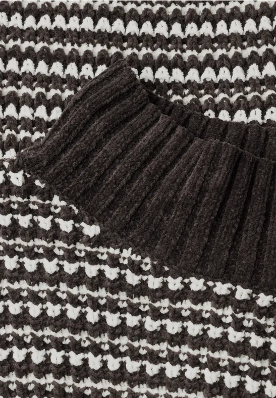 Close-up van een zwart-witte gebreide trui met geribbelde kraag en structuurpatroon.