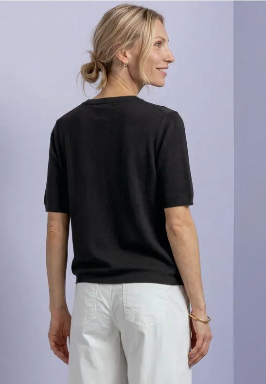 Frau von hinten in schwarzem Kurzarmshirt und weißer Hose, blondes Haar zu einem tiefen Pferdeschwanz gebunden.