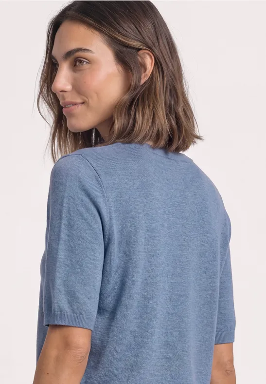 Een vrouw met halflang bruin haar kijkt opzij en draagt een lichtblauw T-shirt.