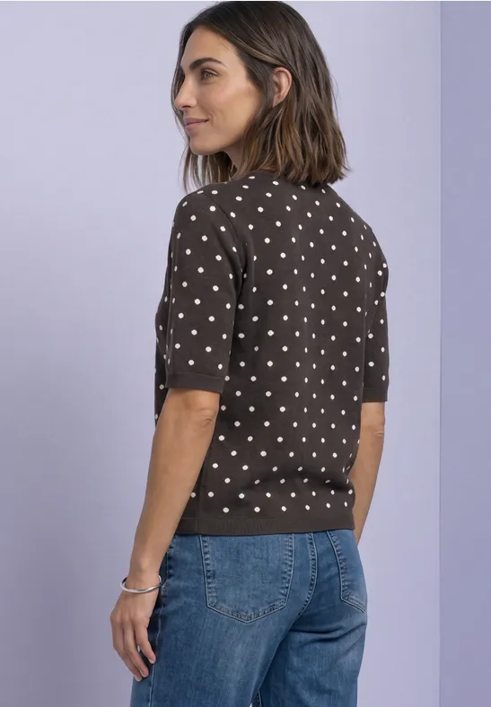 Frau im gepunkteten Kurzarmpullover und Jeans, seitlich stehend.