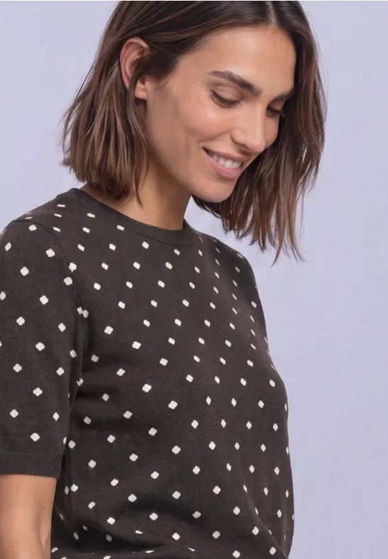 Frau mit braunem, gepunktetem Pullover lächelt seitlich.