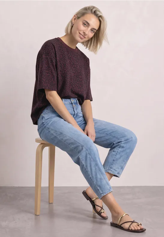 Une jeune femme blonde est assise sur un tabouret, en jean et haut court, regardant l'objectif.