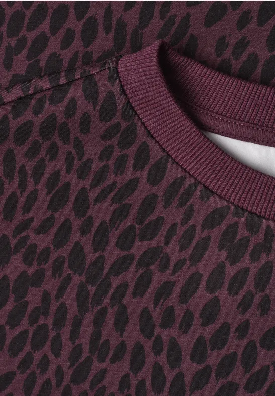 Gros plan sur un pull bordeaux orné d’un motif tacheté organique foncé.